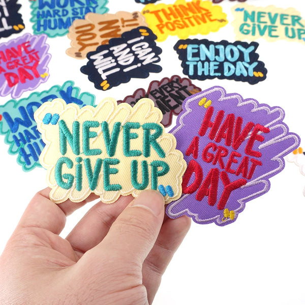A hand holds a purple iron-on embroidered patch that reads Have a Great Day