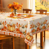 A table covered with a fall harvest pumpkin and maple leaf tablecloth featuring autumn foliage patterns.