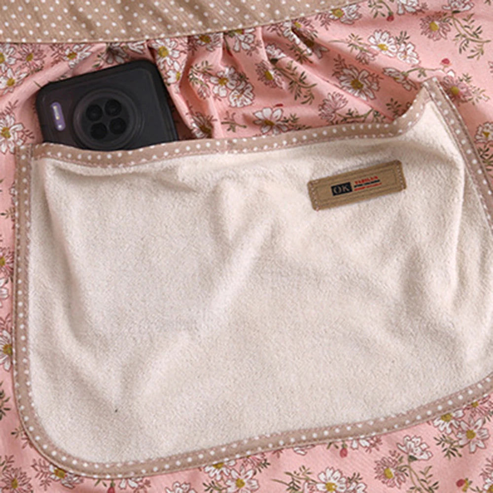 A cream-colored kitchen apron with a floral pattern is shown on a pink fabric background.