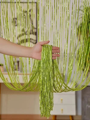 A hand is holding long, shimmering lime green decorative door string curtains that drape down like a curtain.