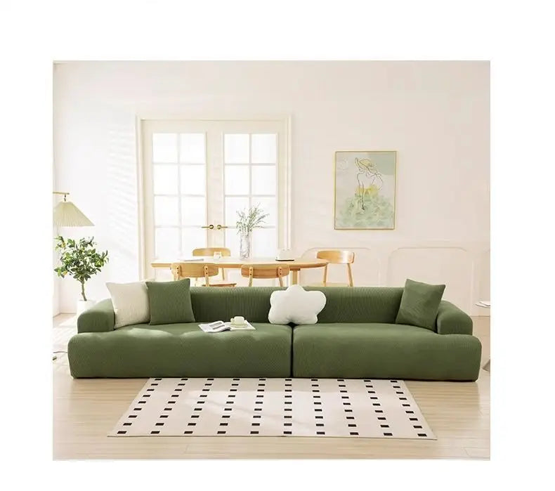 A modern, olive green stretchable full-wrap sofa slipcover in a bright, minimalist living room.