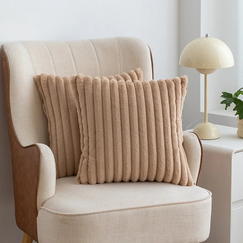A beige faux fur stripe decorative throw pillow cover resting on a cream upholstered armchair.