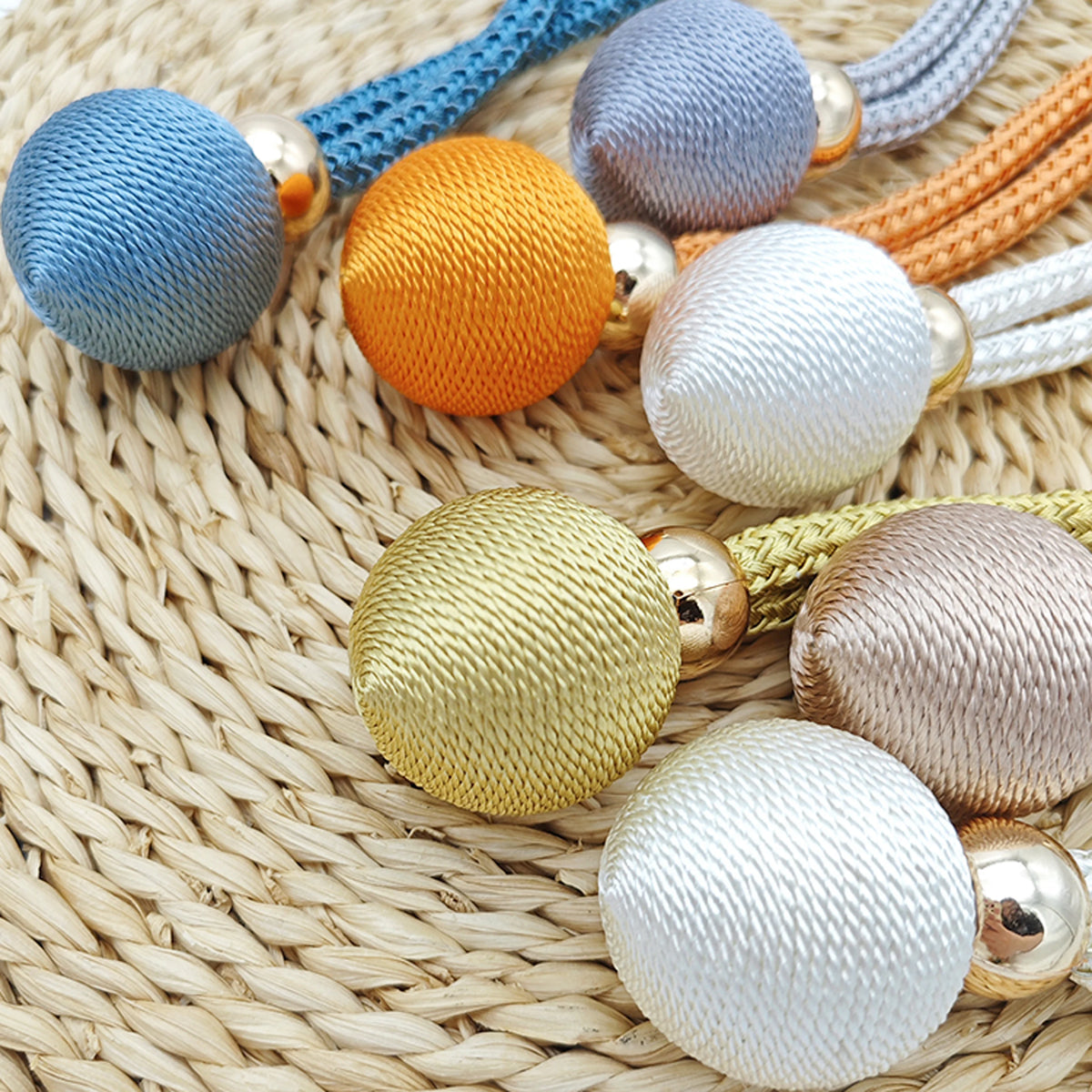 A collection of colorful, textured French ball curtain tiebacks in various shades including blue, orange, silver, and gold.