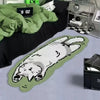 A light green cartoon cat plush rug is displayed on a gray surface next to a black fabric and some glass items.