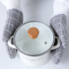 A pair of white heat-resistant kitchen oven gloves with gray checkered fabric are holding a white cooking pot.