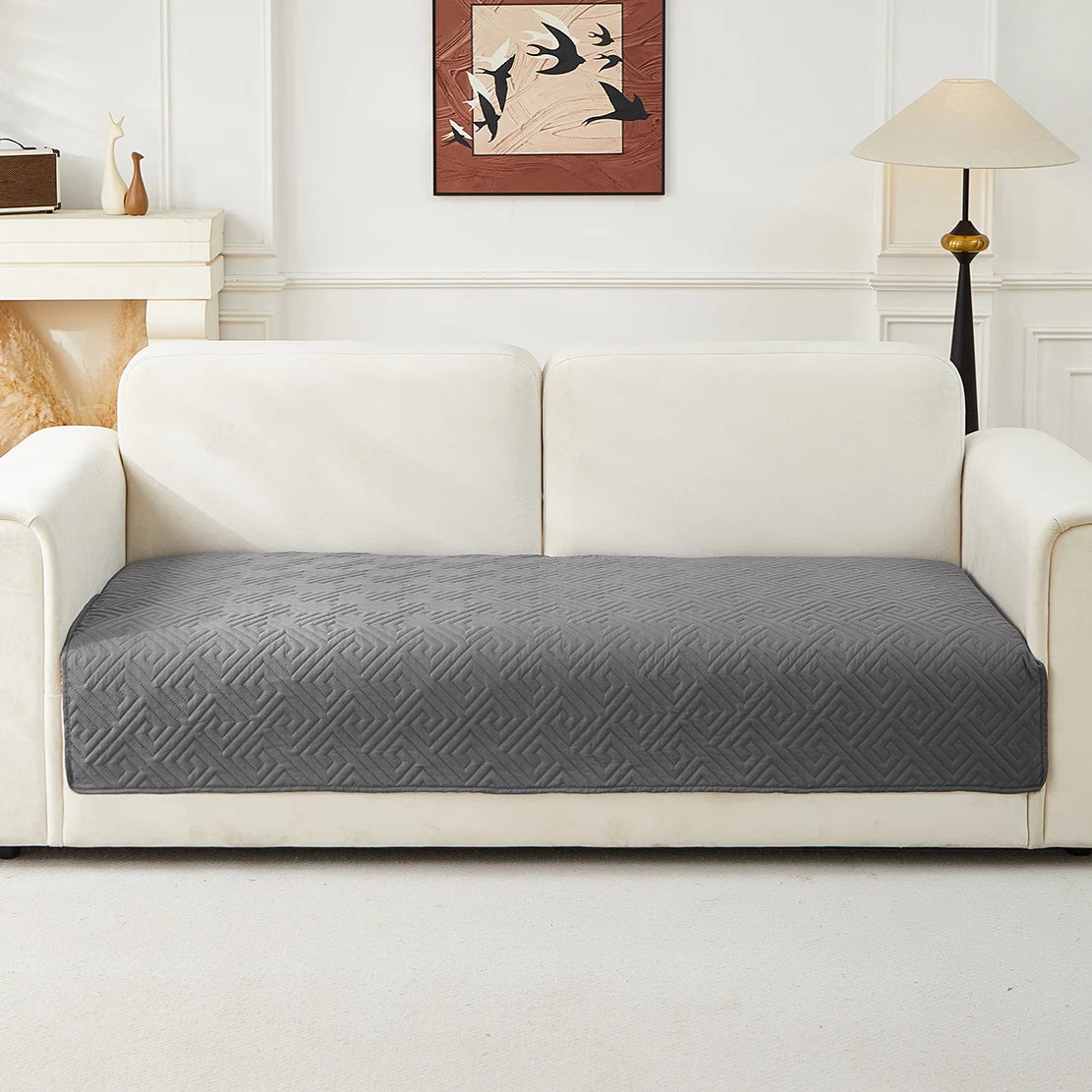 A light beige sofa with a gray geometric quilted cushion cover on a white floor.