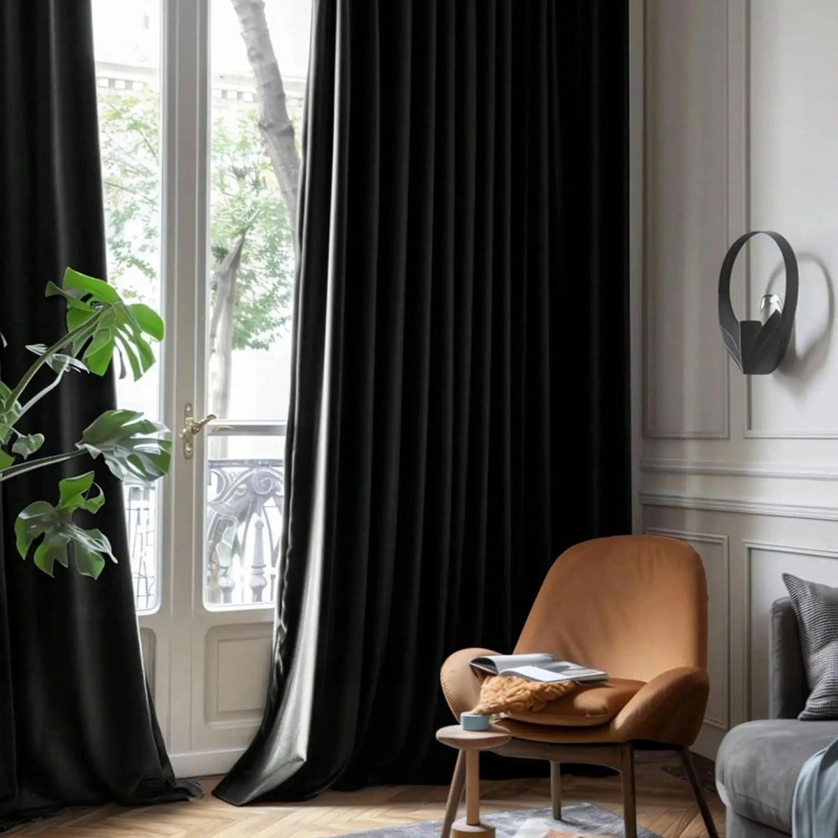 Black velvet blackout curtains hanging in a window with green foliage visible outside.