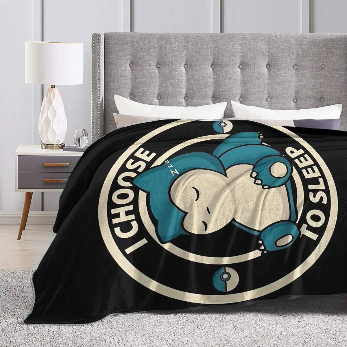 A black throw blanket featuring a light blue sleeping face design on a circular background.