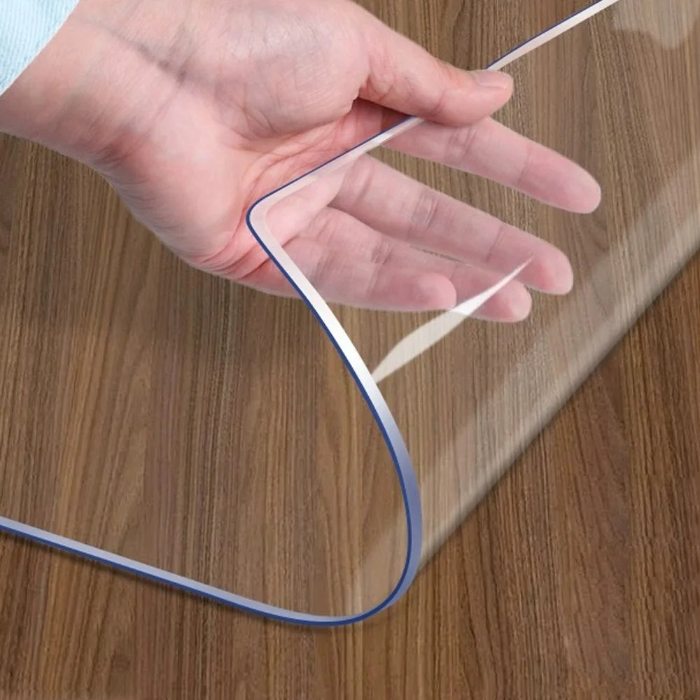 A hand is holding a clear PVC table protector mat, showing its flexible and transparent material.