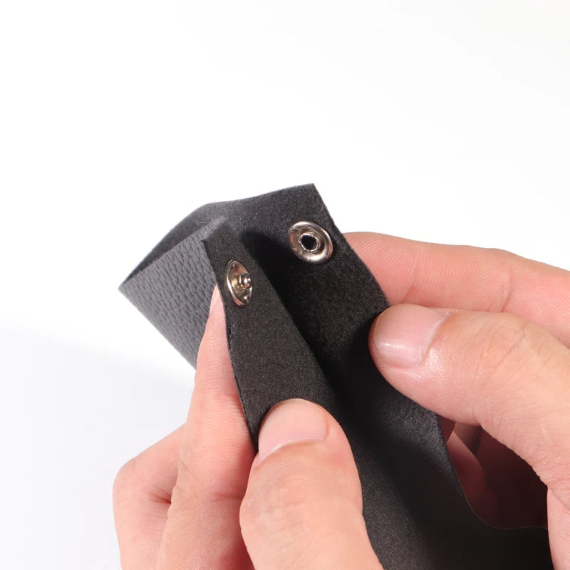 A hand holds a black precision iron snap button, showing its texture and mechanism.