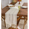 A beige hand-woven table runner is placed on a dark wooden table in a rustic home setting.