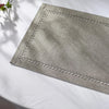 A rectangular linen placemat with a decorative stitched border is placed on a white surface.