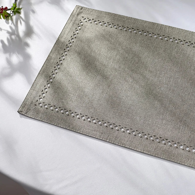 A rectangular linen placemat with a decorative stitched border is placed on a white surface.