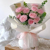A bouquet of pink roses wrapped in white organza ribbon and presented next to a white classical statue.