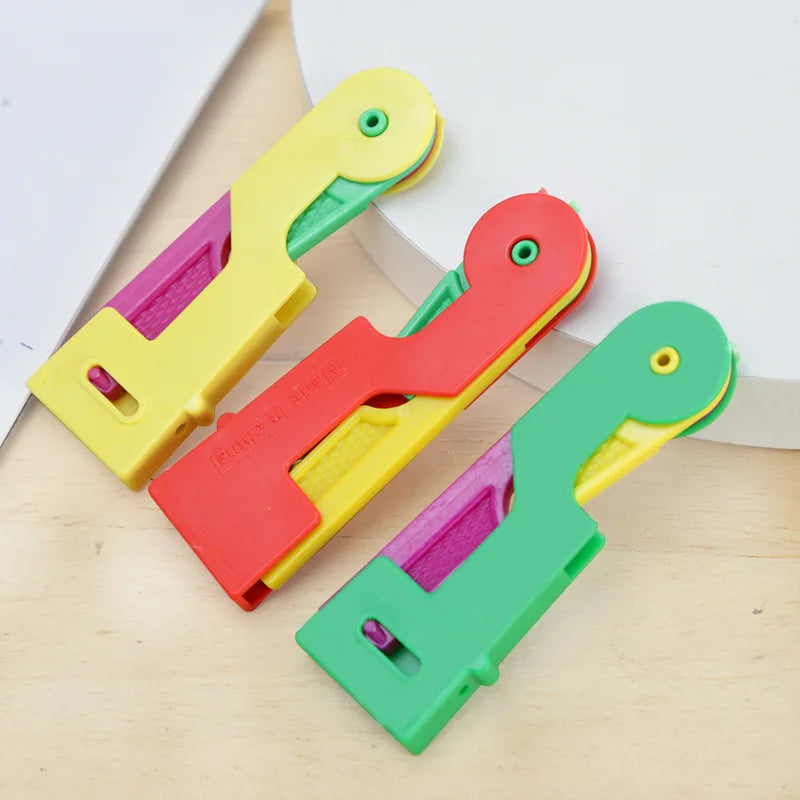 Three automatic sewing needle threaders in yellow, pink, and green plastic are displayed on a wooden surface.