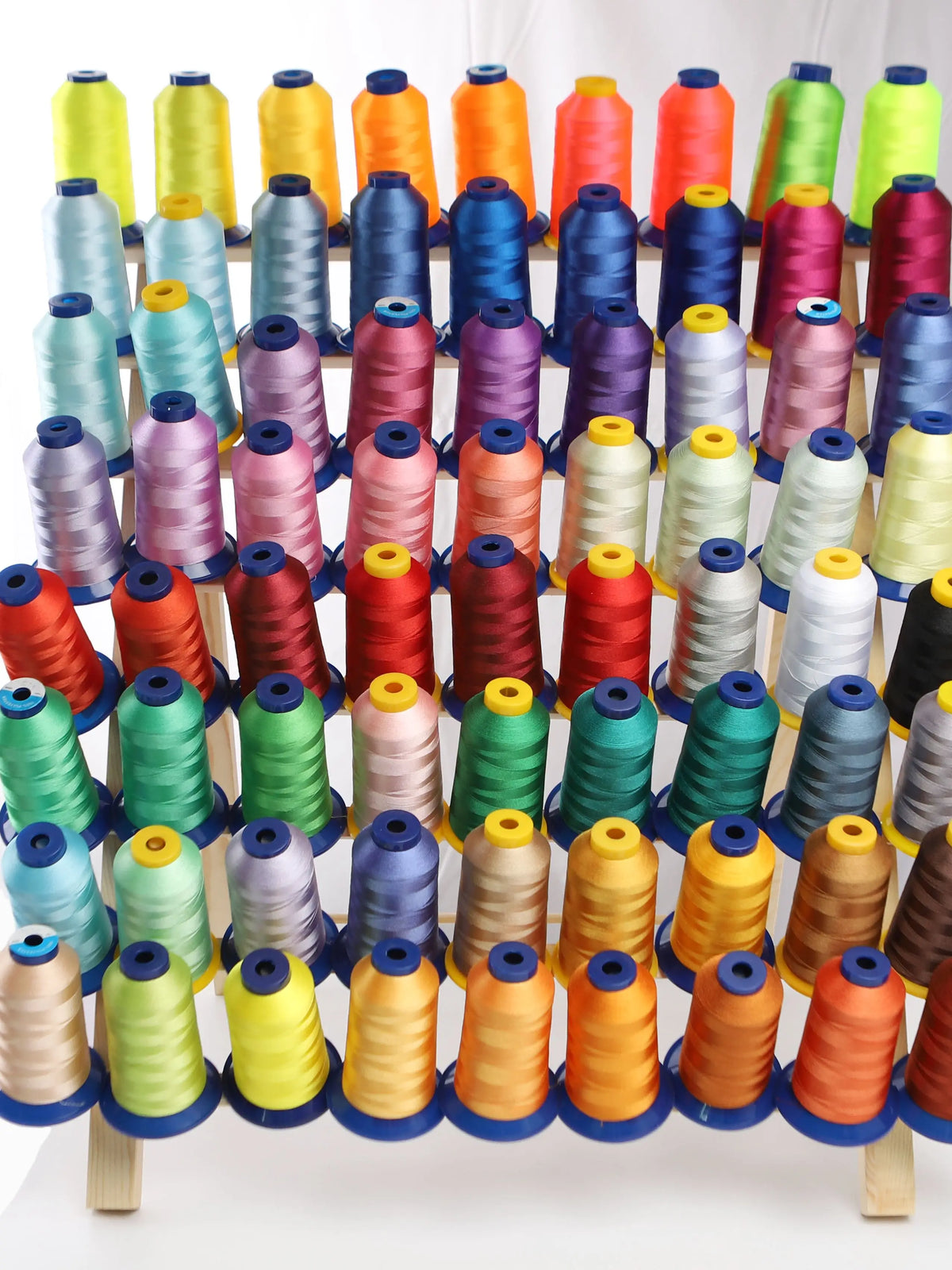 A row of various colored embroidery threads in spools displayed on a wooden rack.