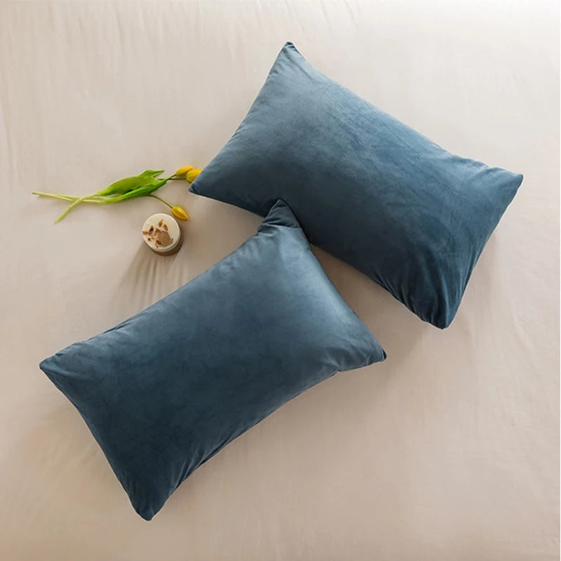 A teal velvet throw pillow is resting on a light-colored surface next to a yellow flower stem.