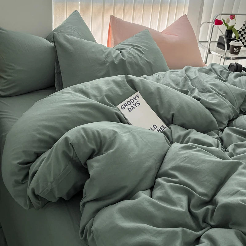 A close-up of a soft sage green duvet cover and pillows with pink accents on a bed.