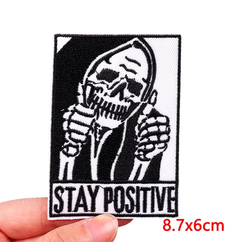 Black and white embroidery patch featuring a skull with hands raised, with the text STAY POSITIVE below.