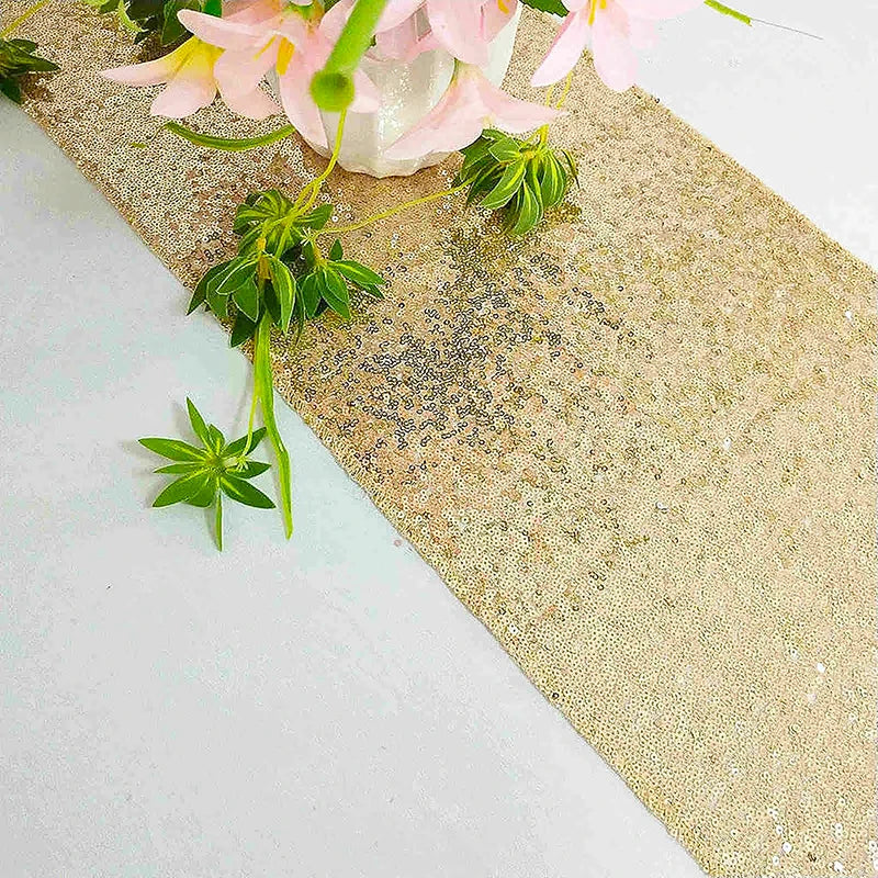 Golden sequin table runner with pink flowers and green foliage on a white surface