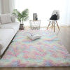 A pink and blue tie-dye shaggy rug is placed on a light wooden floor in a bright living room setting.