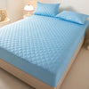 Light blue quilted mattress protector on a bed with matching pillows and a bedside lamp.