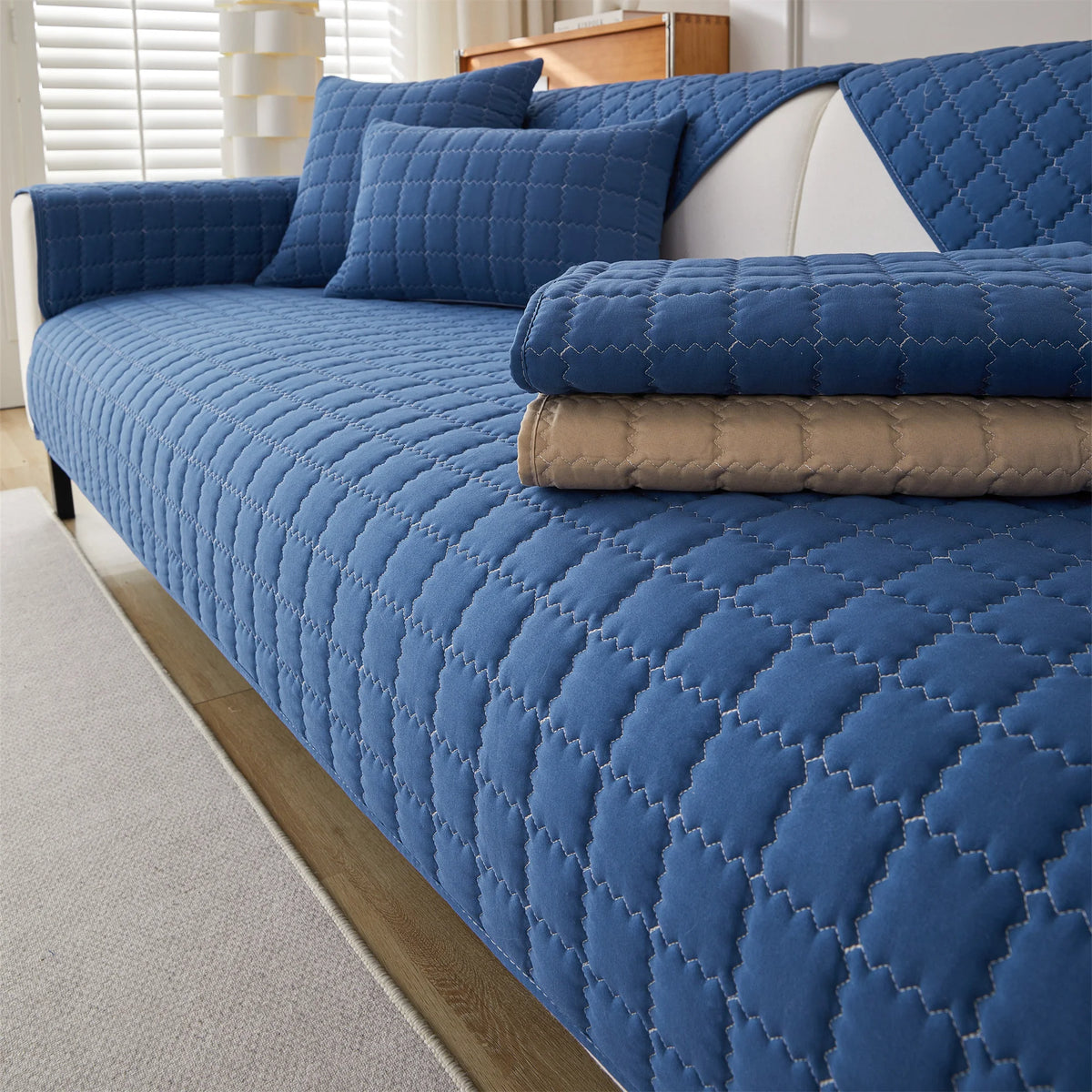 A deep blue quilted anti-slip sofa cover with a plush texture displayed on a sofa.
