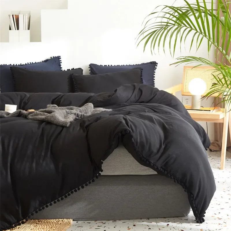 A black duvet cover set with pom-pom decoration displayed on a bed.