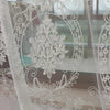 Sheer white embroidered curtains featuring delicate floral and vine patterns in a window setting.