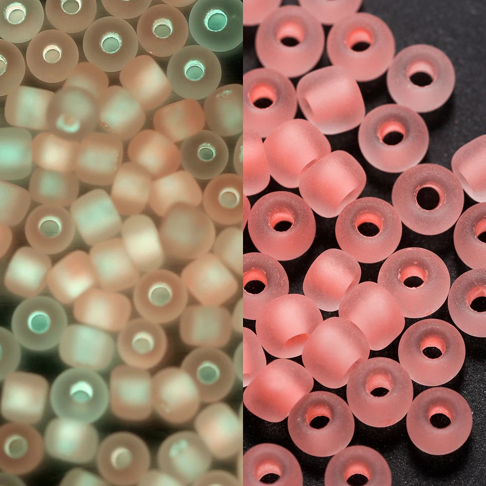 A close-up view of a 600-pack of 3mm glow-in-the-dark glass seed beads in various shades of pink and green.