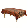 Orange and black zebra print disposable plastic tablecloth spread over a wooden table.