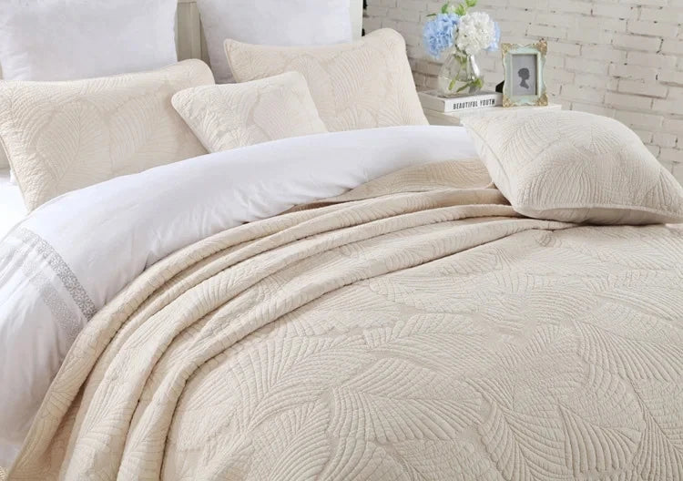 A set of cream embroidered cotton quilted pillow covers and a matching blanket on a bed.