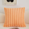 An orange faux fur stripe decorative throw pillow cover resting on a light-colored sofa.