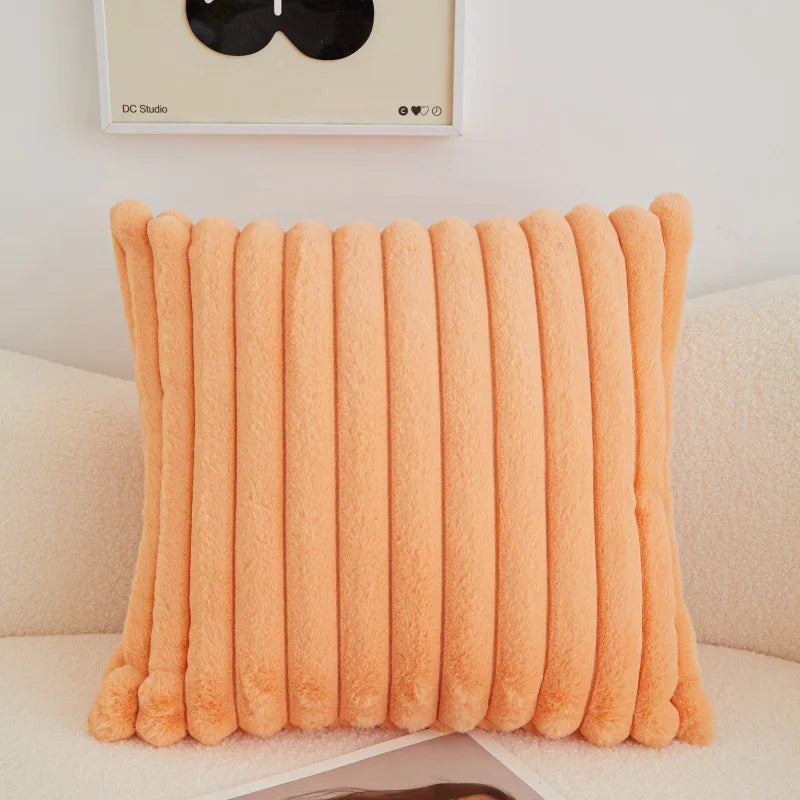 An orange faux fur stripe decorative throw pillow cover resting on a light-colored sofa.