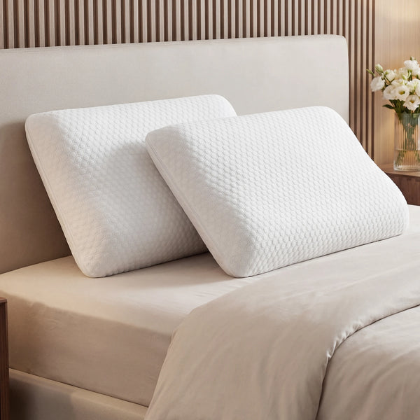 A white memory foam neck pillow resting on a beige bed with light wood paneling in the background.