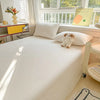 A white organic cotton bedding set with a flat sheet and pillow, featuring a small teddy bear decoration.