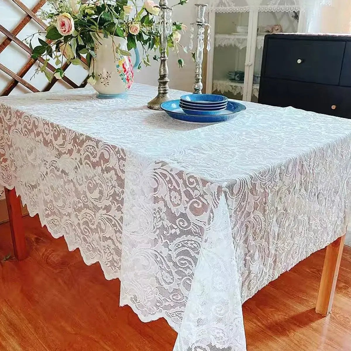 A white vintage lace tablecloth covers a rectangular dining table set for a meal.