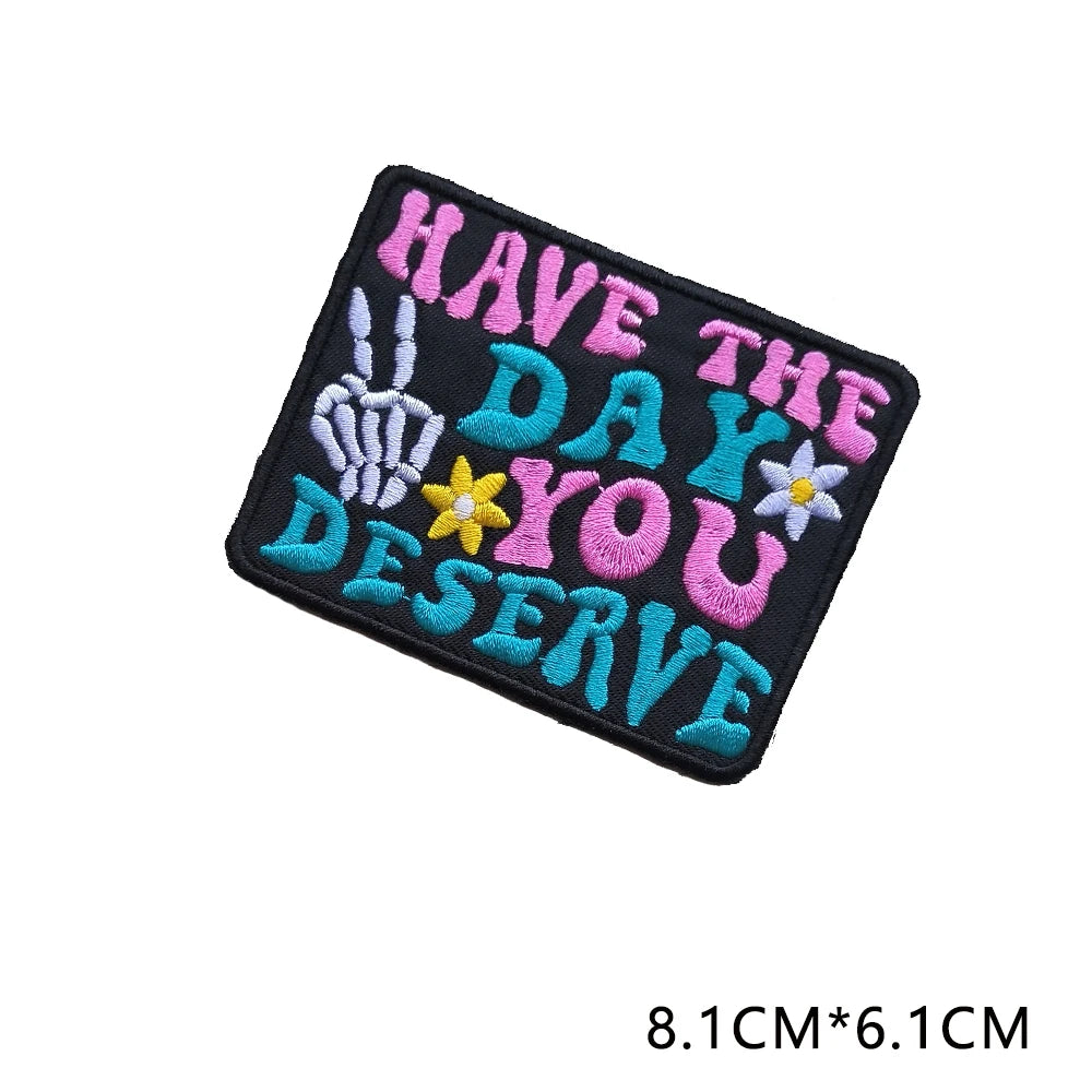 Black iron-on embroidered letter patch with the text HAVE THE DAY YOU DESERVE in purple, teal, and yellow thread.