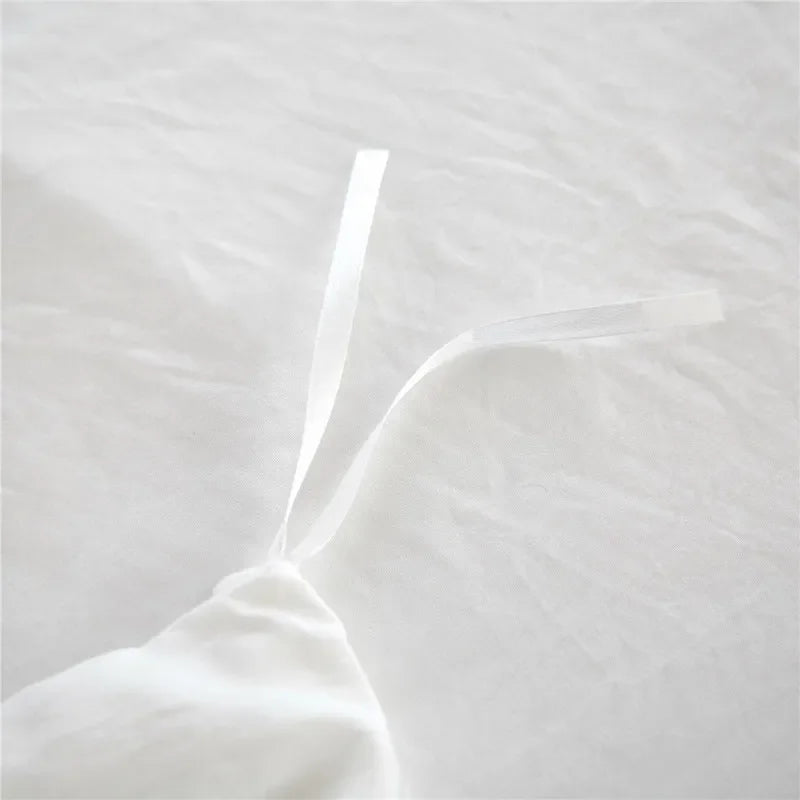 A white duvet cover set with a soft, gathered fabric and a clear plastic tie visible on a white bed.