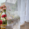 A sheer floral lace curtain panel hangs next to a potted pink flower arrangement.