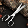 A pair of professional stainless steel sewing scissors resting on a dark surface next to a piece of bark.