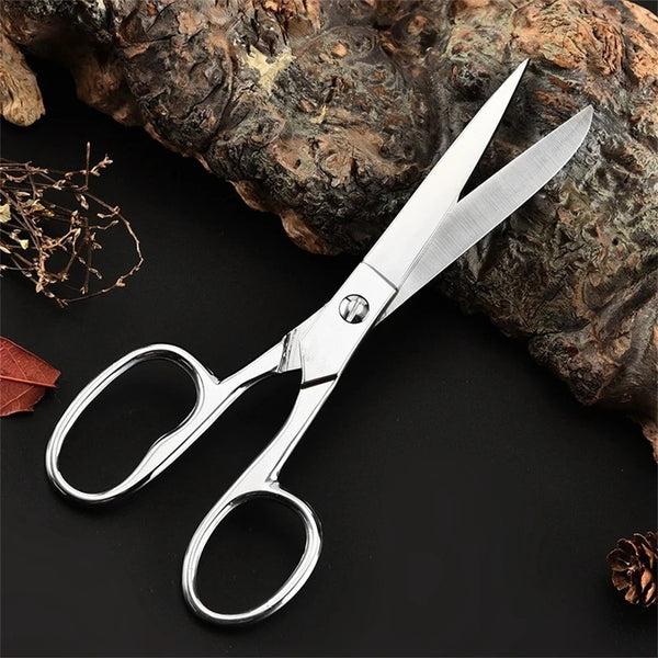 A pair of professional stainless steel sewing scissors resting on a dark surface next to a piece of bark.