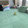 A light green plush interlocking puzzle rug mat with various textured cushions and a stuffed animal on a wooden floor.