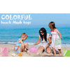 A mother and child are sitting on the beach with colorful mesh bags.
