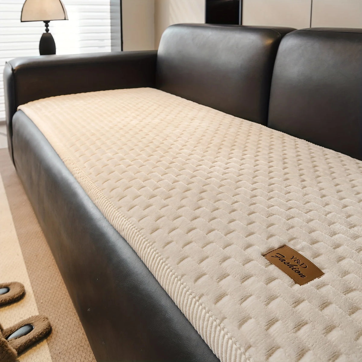 A dark leather sofa with a beige quilted cushion and a matching brown leather accent tag.