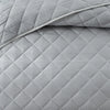 A close-up of a light gray quilted bedspread featuring diamond stitching.