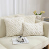A collection of white, textured plush throw pillows with a geometric weave pattern displayed on a light-colored sofa.
