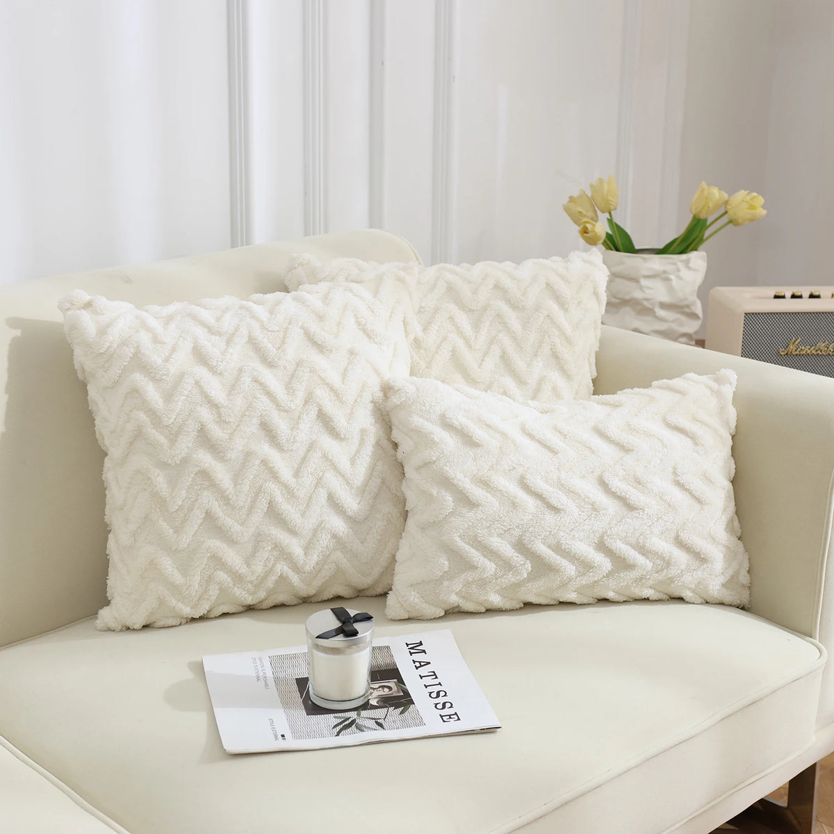 A collection of white, textured plush throw pillows with a geometric weave pattern displayed on a light-colored sofa.