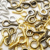 A close-up of various silver and gold eye screw pins for jewelry making scattered on a white surface.