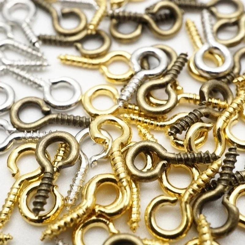 A close-up of various silver and gold eye screw pins for jewelry making scattered on a white surface.